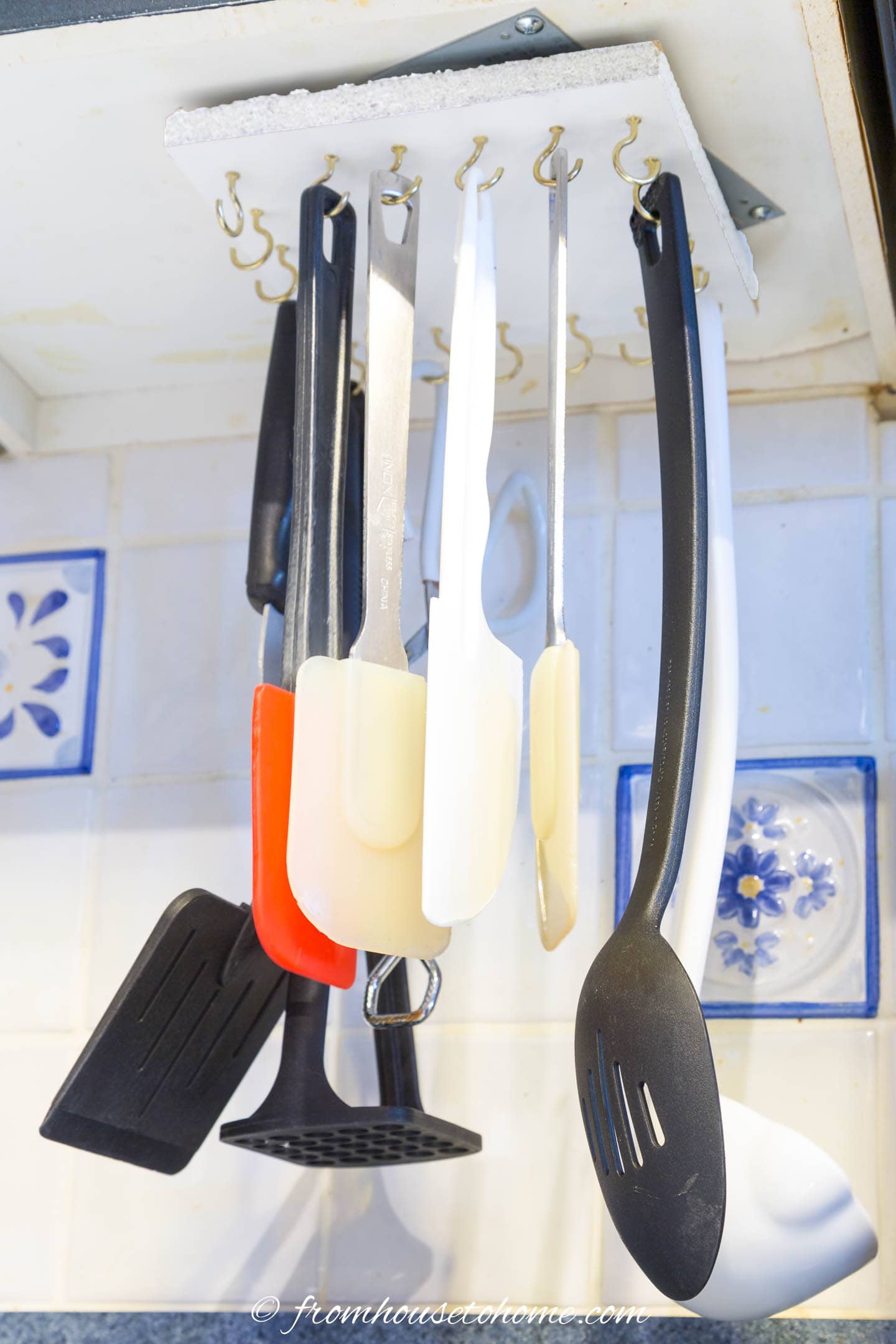 utensils hanging under kitchen cupboard on gold hooks