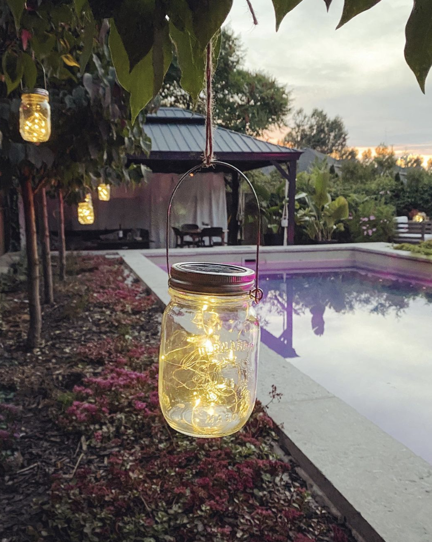 mason jar with string lights inside hanging from tree by pool