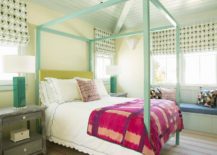 calloped bedding topped with a red and purple blanket accents a turquoise blue canopy bed finished with a yellow headboard complementing pale yellow walls. The bed is flanked by green lamps placed on gray nightstands beneath windows dressed in yellow and blue roman shades