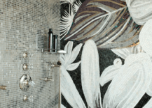 walk-in shower with mosaic tile surround framing dual shower heads with crystal faucet alongside accent wall tiled in a large scale black, gray and gold floral mosaic.