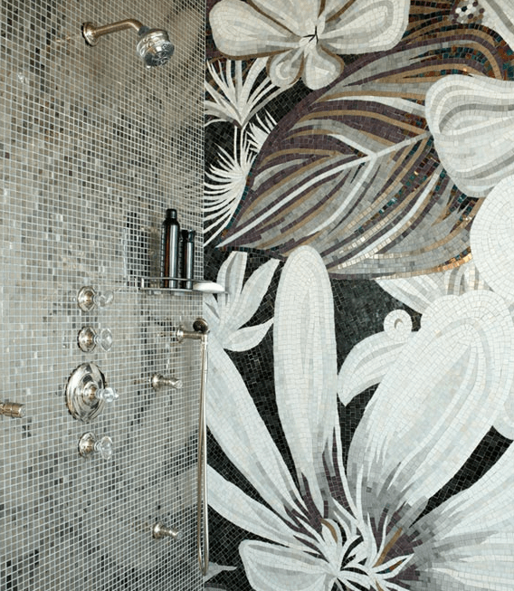walk-in shower with mosaic tile surround framing dual shower heads with crystal faucet alongside accent wall tiled in a large scale black, gray and gold floral mosaic.