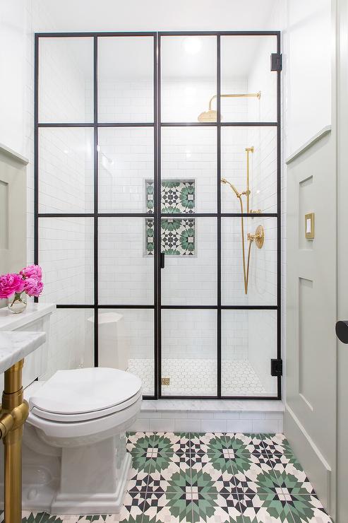 Green and black mosaic cement bathroom floor tiles toilet steel and glass shower enclosure walk-in shower with a brass rain shower kit fixed over white hexagon floor tiles and white subway surround tiles framing a green and black mosaic cement tiled shelf