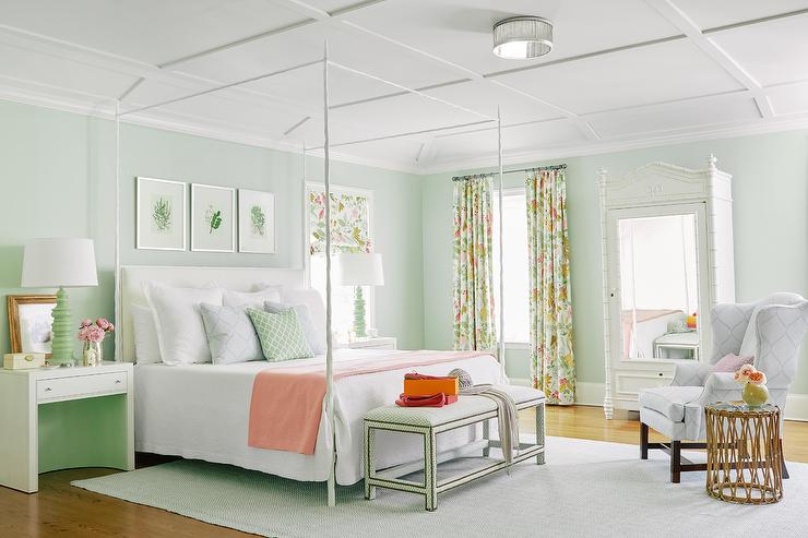 Pastel-colored bedroom is accented with spring green walls and a white coffered ceiling Three art pieces hang over a white canopy bed finished with a white upholstered headboard and white bedding accented with a peach-colored throw blanket