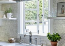 pattern roman shades hanging over white kitchen window pattern wallpaper white apron farmhouse sink open shelving potted plant on counter