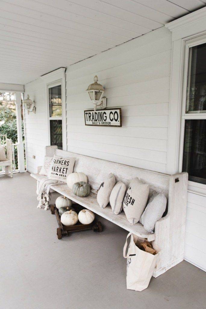 white porch pew with pillows and pumpkins along white sided house