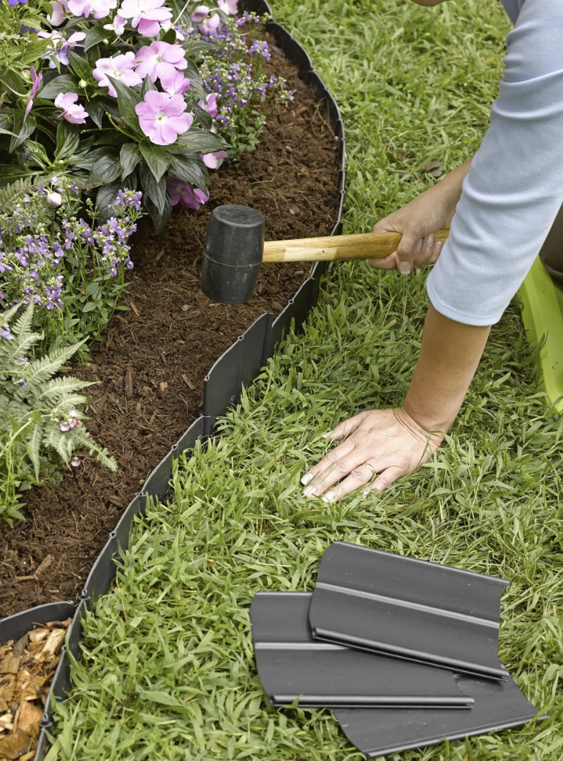 woman pounding in plastic lawn edging between garden bed and grass