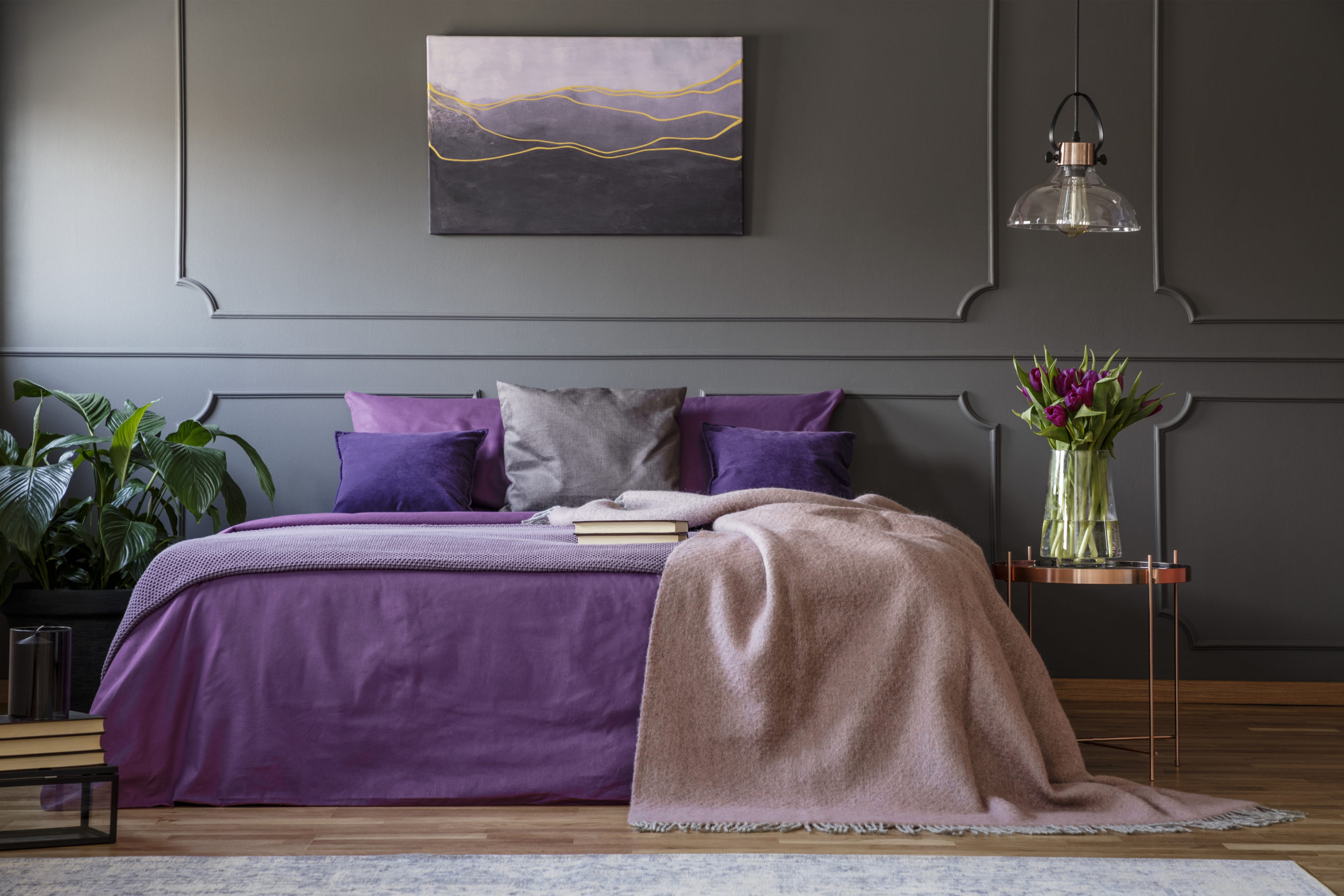 Lamp above copper table with flowers next to bed with violet bedding in purple bedroom interior