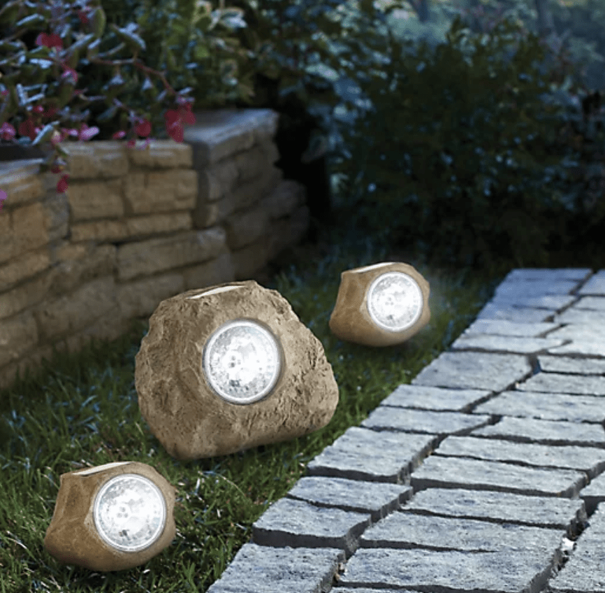 Landscape solar lights inside fake rocks on garden path at night