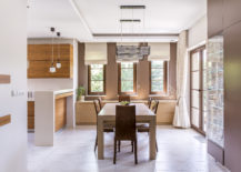 Kitchen and dining room in modern house with wood table and chairs three long skinny windows wood cupboards and sleek design contemporary chandelier