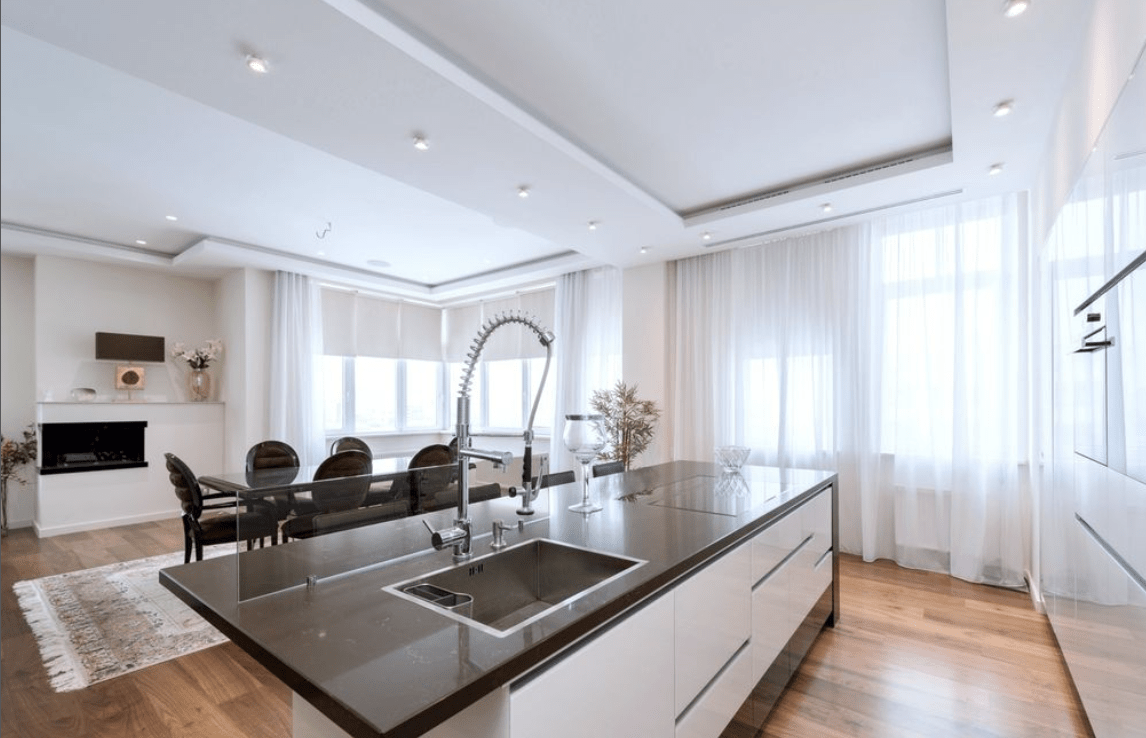 large open kitchen with black granite countertops gooseneck faucet white kitchen sheers table in background with black chairs modern