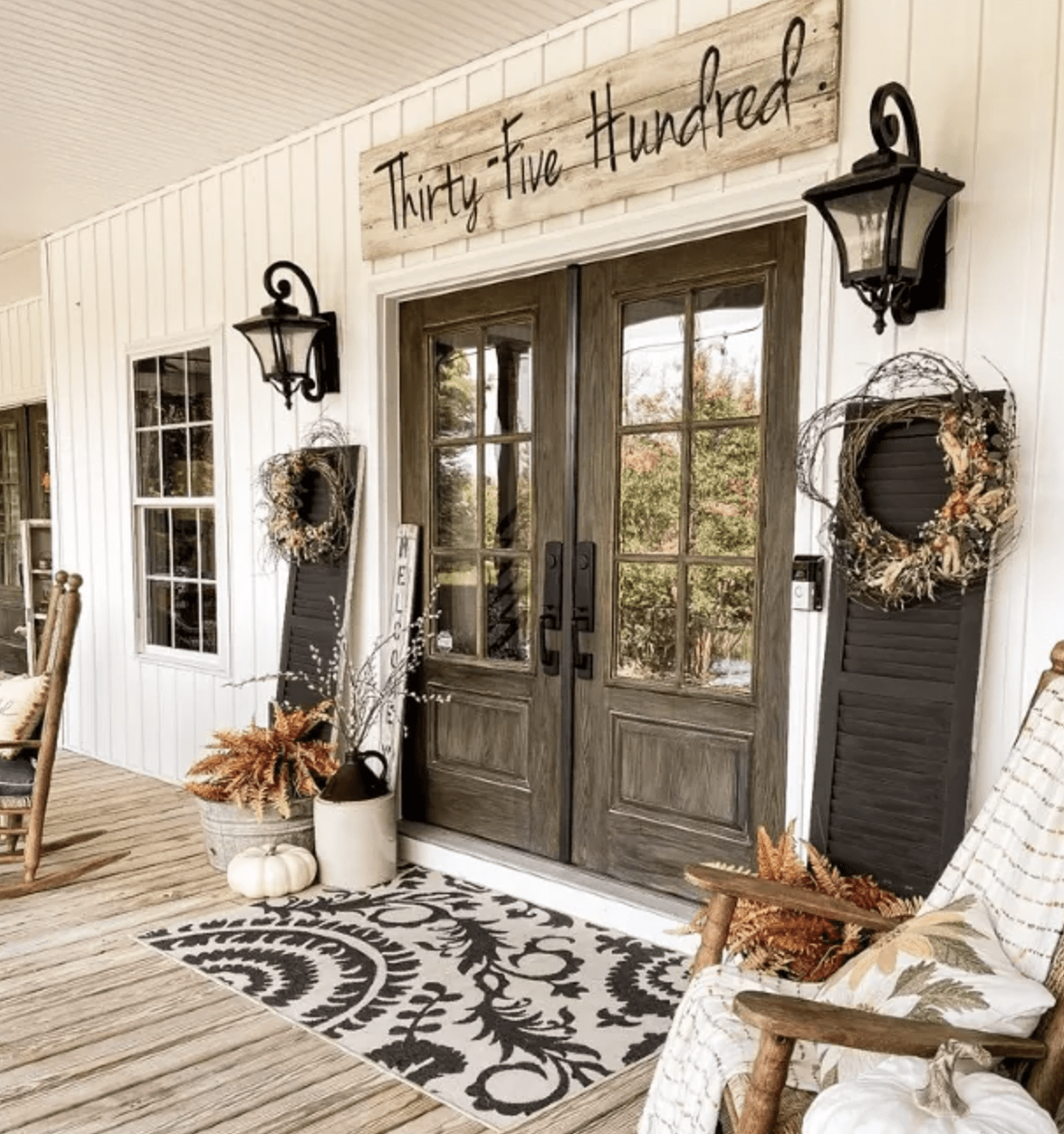 front porch with double wood doors sign over top black lanterns and shutters with wreaths fall decorated