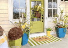 bright yellow decor on a porch decorated for spring green striped doormat basket on door black farmhouse exterior wall sconces large blue planters