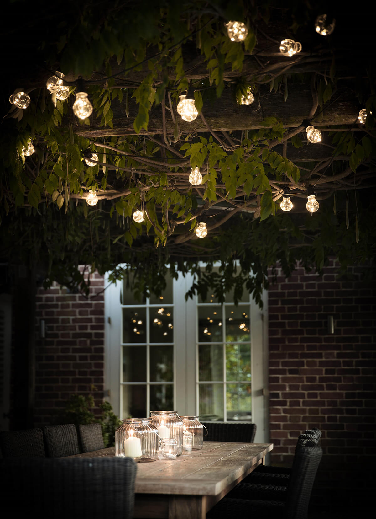 string lights edison bulbs in tree light up at night above table with candles in lanterns