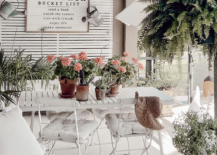 white patio furniture on porch with farmhouse style sign on wood slat wall fern potted plants on table pillows