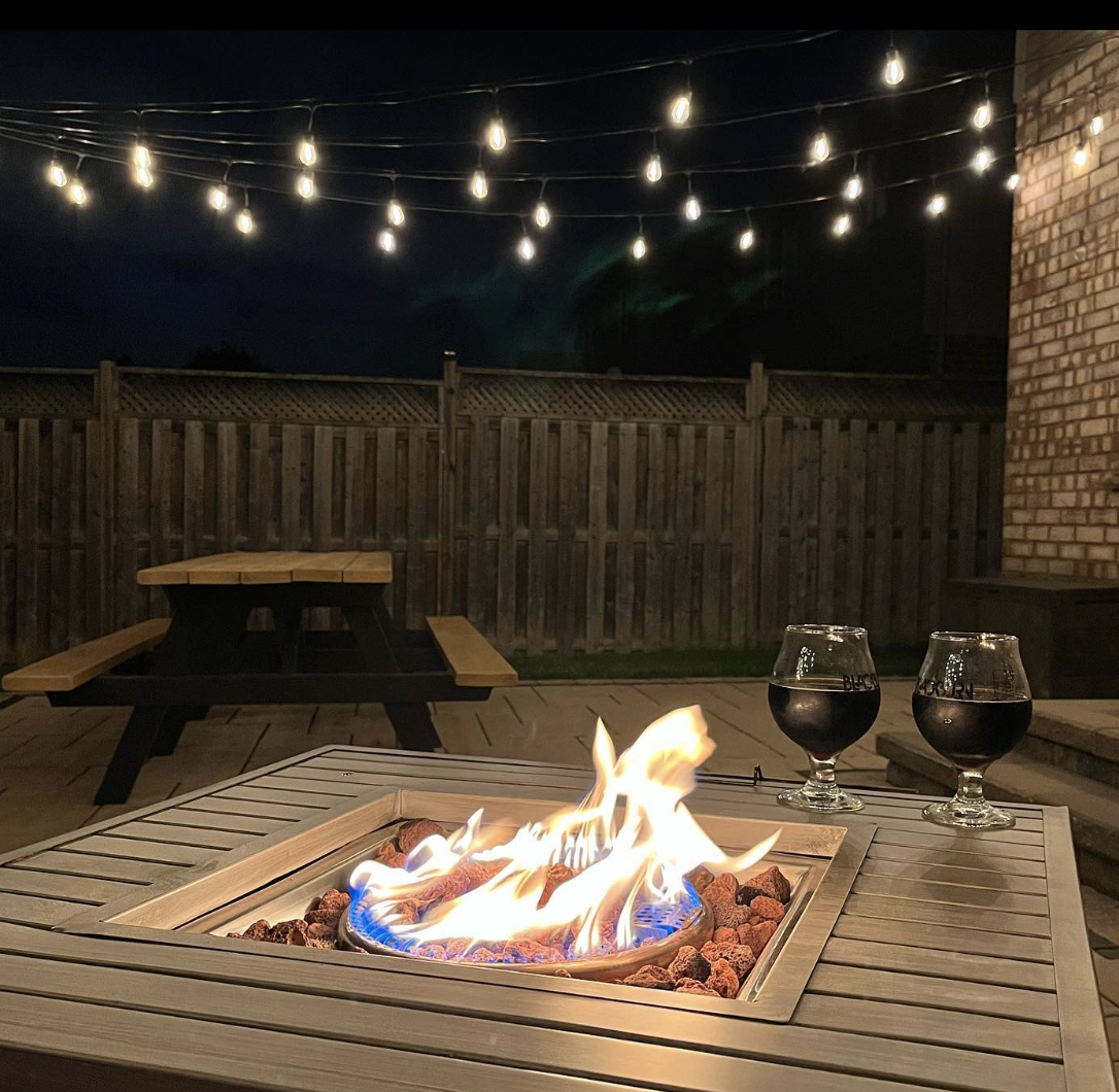 close up of table top fire bowl two glasses of red wine string lights night time