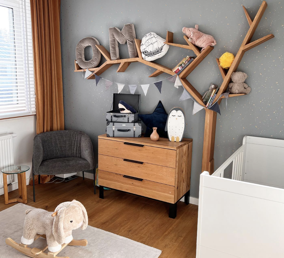 wood branch decorative shelf on wall in nursery with stuffed animals on it wood dresser and grey chair in corner