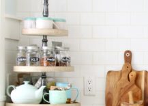 three tiered tray with spice jars on them mugs and teapot white subway tile background next to wood handle cutting boards