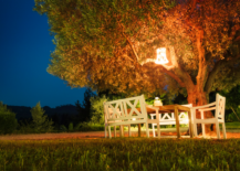 lantern lit up in tree with table and chairs beneath outside backyard