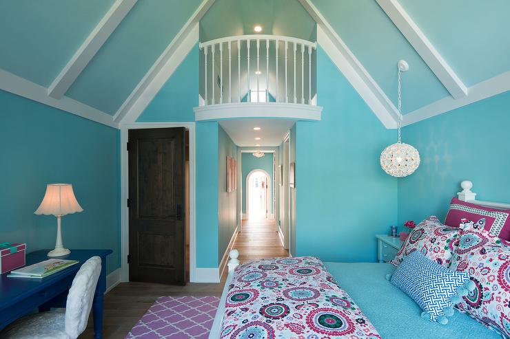 blue and pink girl's bedroom white wood bed dressed in pink and blue suzani style bedding accented with a blue lumbar pillow placed in front of pink and blue suzani style shams white flower light hangs from a blue vaulted ceiling above a blue nightstand pink trellis rug sits in front of the bed and behind a white faux fur chair placed at a blue desk