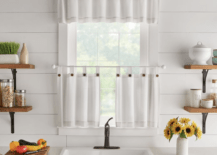 one kitchen window in white bright kitchen with black faucet farmhouse apron sink sunflowers in vase on counter open shelving