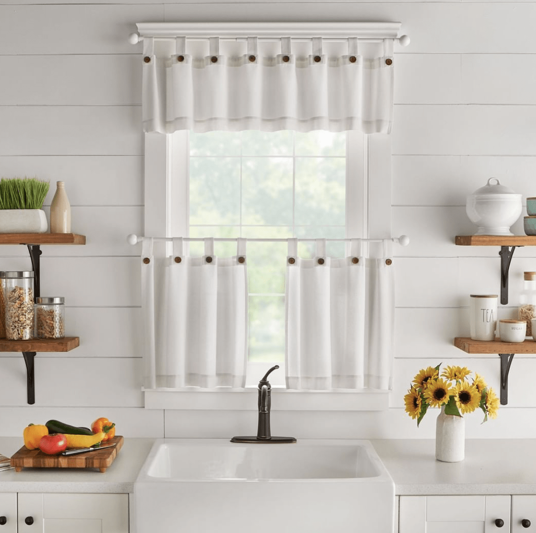 one kitchen window in white bright kitchen with black faucet farmhouse apron sink sunflowers in vase on counter open shelving