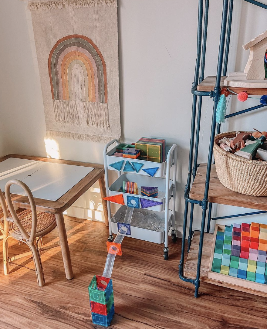 blue rolling cart being used as toy storage in toy room with rainbow hanging wall art small table and chair for kid