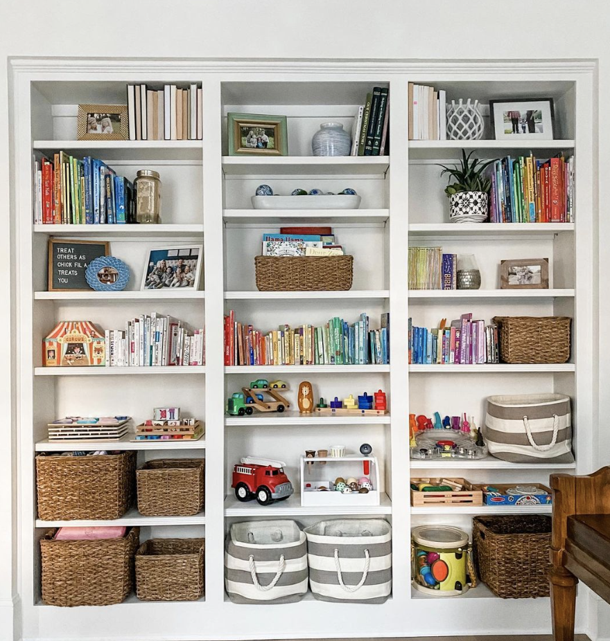 white bookcase filled with colorful books and kids toys seagrass baskets