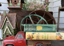 red vintage truck with old books stacked on back rusty wagon wheels and birdhouses behind