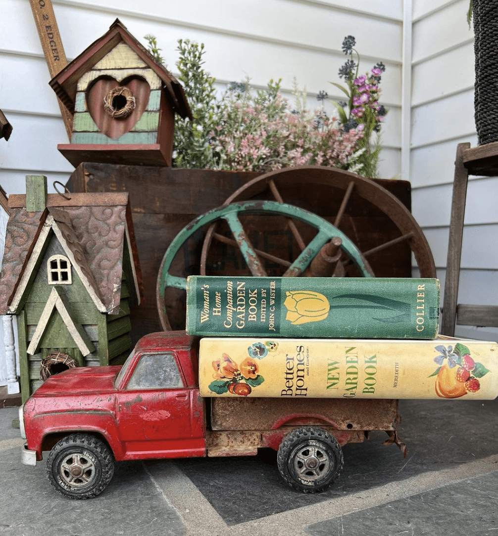 red vintage truck with old books stacked on back rusty wagon wheels and birdhouses behind