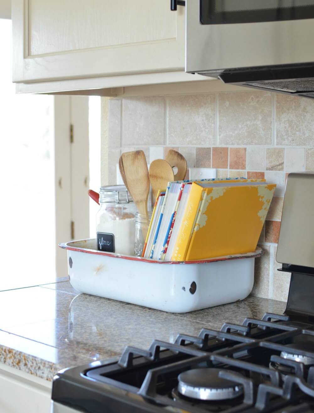 old vintage washpan holding cookbooks on granite countertop next to stove