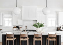 black island in white kitchen with hanging pendants cabinetry stools wicker and wood greenery on countertop