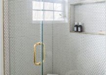 White hexagon shower wall and floor tiles matched with gray grout in a walk in show frameless glass door and a brass door handle
