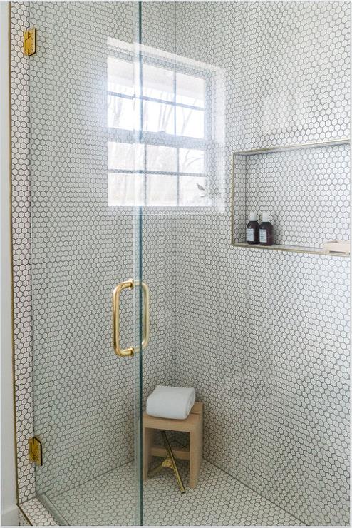 White hexagon shower wall and floor tiles matched with gray grout in a walk in show frameless glass door and a brass door handle