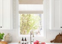 white wood shade window behind white farmhouse apron sink white shaker cabinets black wall sconce flowers in sink