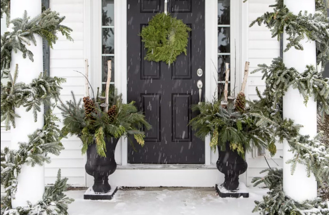 black front door winter porch snowing side by side black urns with winter greenery cedar wreath