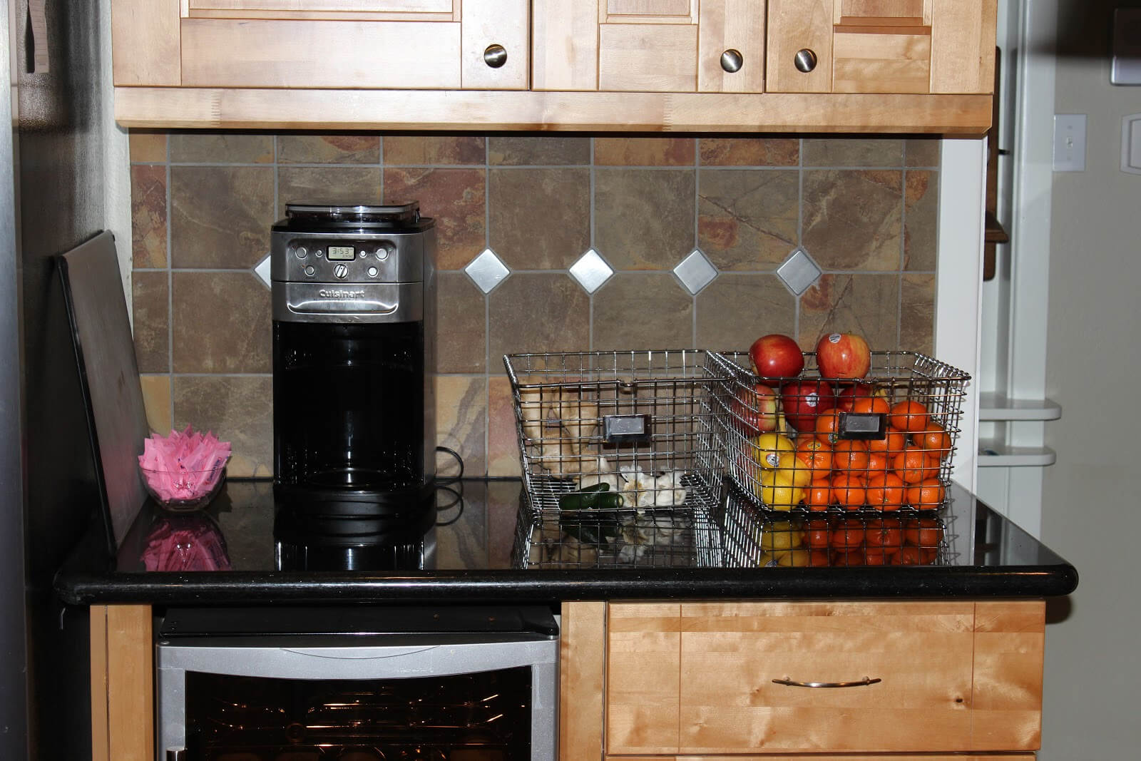black kitchen countertop with light wood cabinets wire baskets on counter with fruits coffee maker