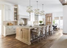 Pendants hang over a distressed kitchen island accented with a rustic stone countertop. A row of four wicker barstools sit at the island facing a sink