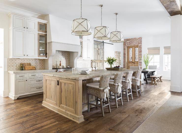 Pendants hang over a distressed kitchen island accented with a rustic stone countertop. A row of four wicker barstools sit at the island facing a sink