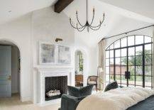 large primary bedroom with black chandelier fireplace black frame arch window with doors