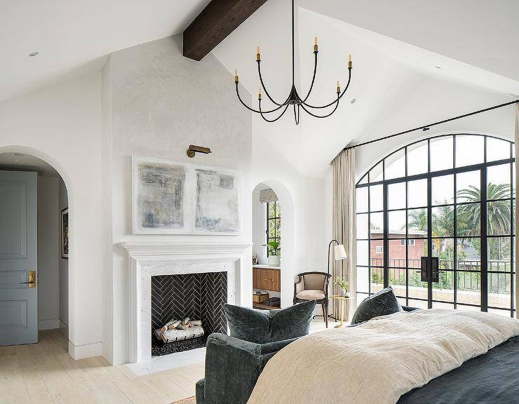 large primary bedroom with black chandelier fireplace black frame arch window with doors