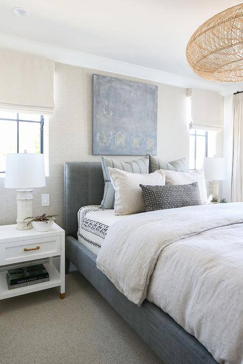 blue and white bedroom with large velvet bed utopian art hanging over bed white roman shades in window nightstand and white table lamps