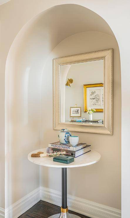 Entryway features an arched alcove with a silver leaf beaded mirror over a round marble top accent table.
