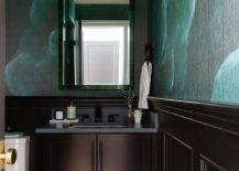 Chic contemporary green and black powder room features walls clad in green and black wallpaper accented with black wainscoting and a black shaker washstand donning a black marble countertop. The washstand is finished with a matte black faucet kit mounted under a malachite mirror.