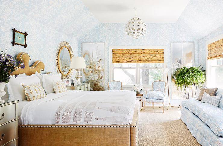 Blue and beige bedroom with a burlap bed flanked by silver nightstands. A blue sofa faces the burlap bed complimenting accent chairs and bedroom wallpaper.