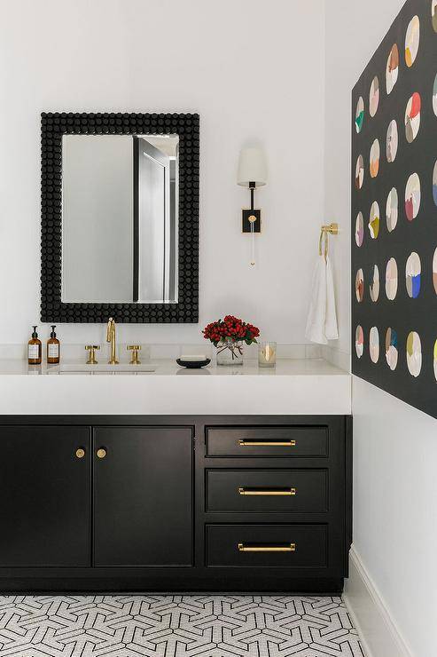 Contemporary bathroom features a black bath vanity with brass gooseneck faucet under a black penny tiled mirror and light gray and black mosaic tiles.