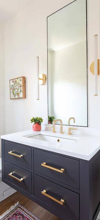 Bathroom features gold pulls on a black floating sink vanity with a white countertop and a brushed gold gooseneck faucet under a tall black vanity mirror flanked by long white and brass sconces.