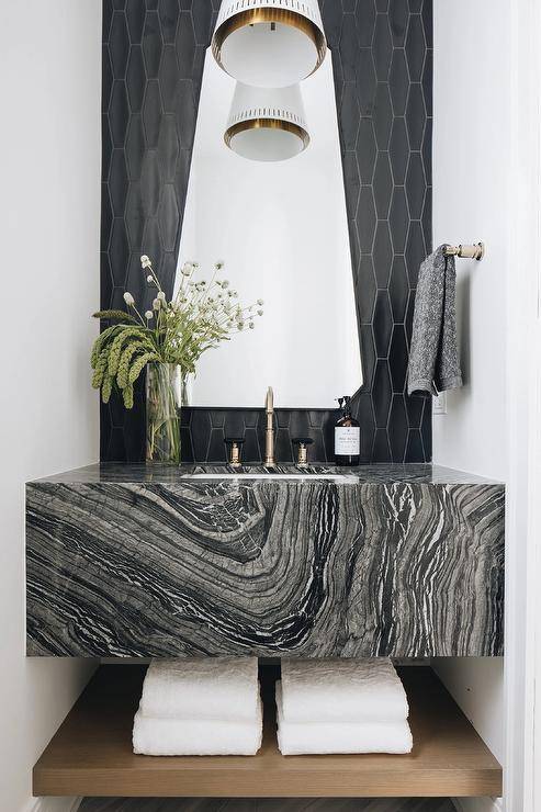 Contemporary black marble floating sink vanity with towel shelf sits under a triangle mirror on black geometric tiles.