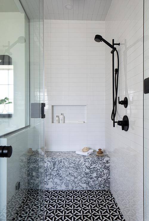 black and white marble tile bench in walk in shower with black faucets white subway tile and mosaic floor tiles glass door