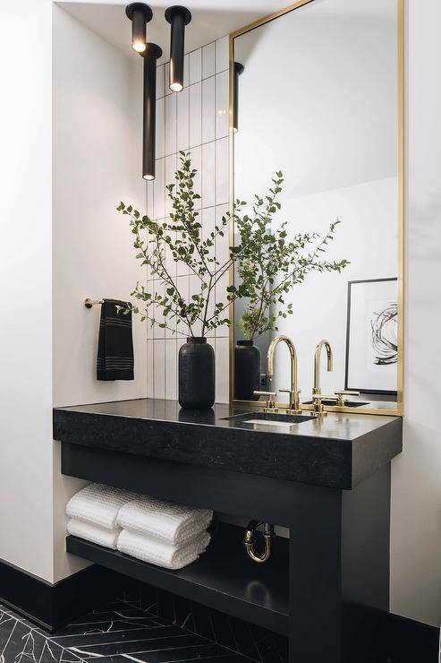 Gold and black master bathroom features a tall brass mirror over a black marble sink vanity with a towel shelf and brass faucet.