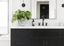 Black pulls on a black washstand vanity balanced with stunning white marble countertop and a matte black gooseneck faucet. A black metal framed mirror keeps the black and white theme with a sleek thin frame flanked by contemporary black and white sconces.